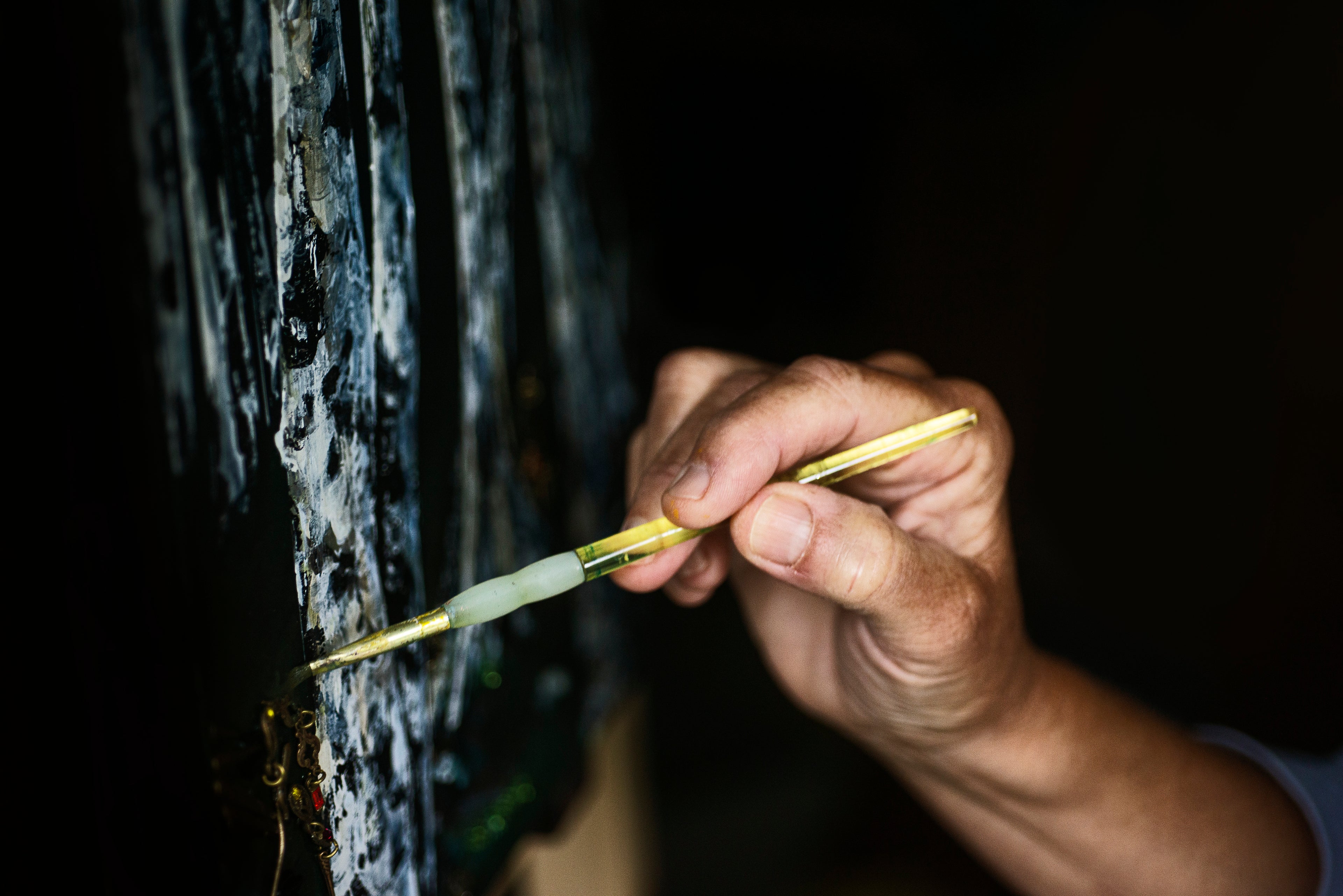 Hands hold a yellow paint brush to a painting of trees